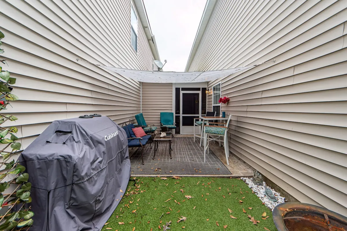 A patio setup with comfortable furniture, a grill, and surrounding greenery, suggesting possibilities for outdoor dining, socializing, or simply enjoying the fresh air.