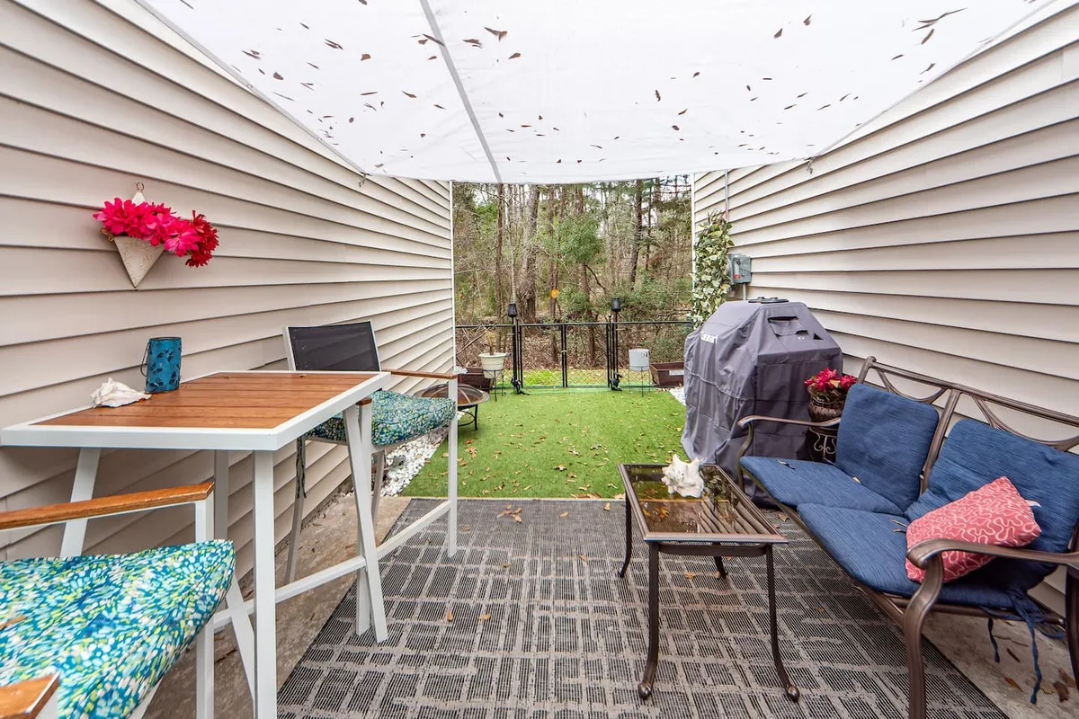 This image features a cozy outdoor seating area with a grill, decorative flowers, and a lush green lawn—an ideal setting for relaxing, entertaining, or enjoying a morning coffee. The image exudes a casual, cozy mood and openness to the outdoors.