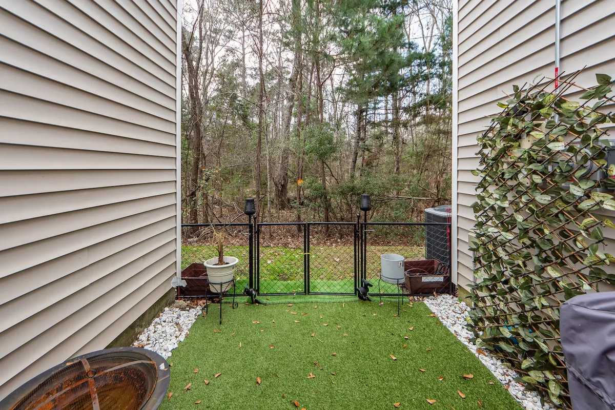 A serene outdoor area featuring artificial grass, a tidy fence, potted plants, and a wooden planter. The space is lush with greenery and designed for peaceful relaxation or small gatherings.