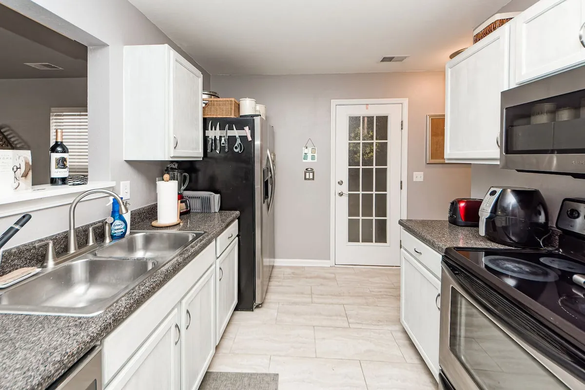 The kitchen area features stainless steel appliances, a double sink, and a central island, conveying a welcoming and functional space designed for everything from holiday feasts to intimate dinners.