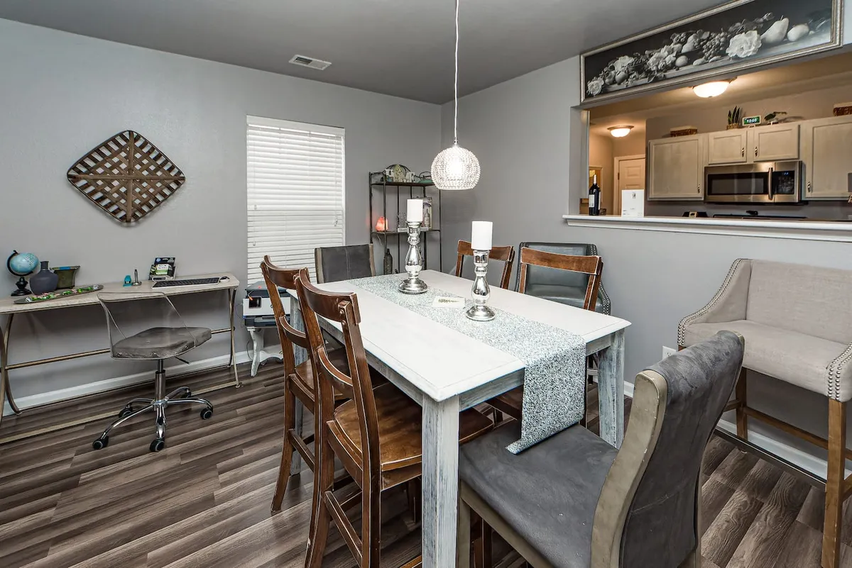 A stylish, multifunctional interior space featuring a modern dining table adorned with a statement chandelier, an office desk setup ideal for productive work-from-home sessions, and decorative wall art that adds a contemporary touch. The setting invites both shared meals and focused productivity, all within a single, cohesive area.